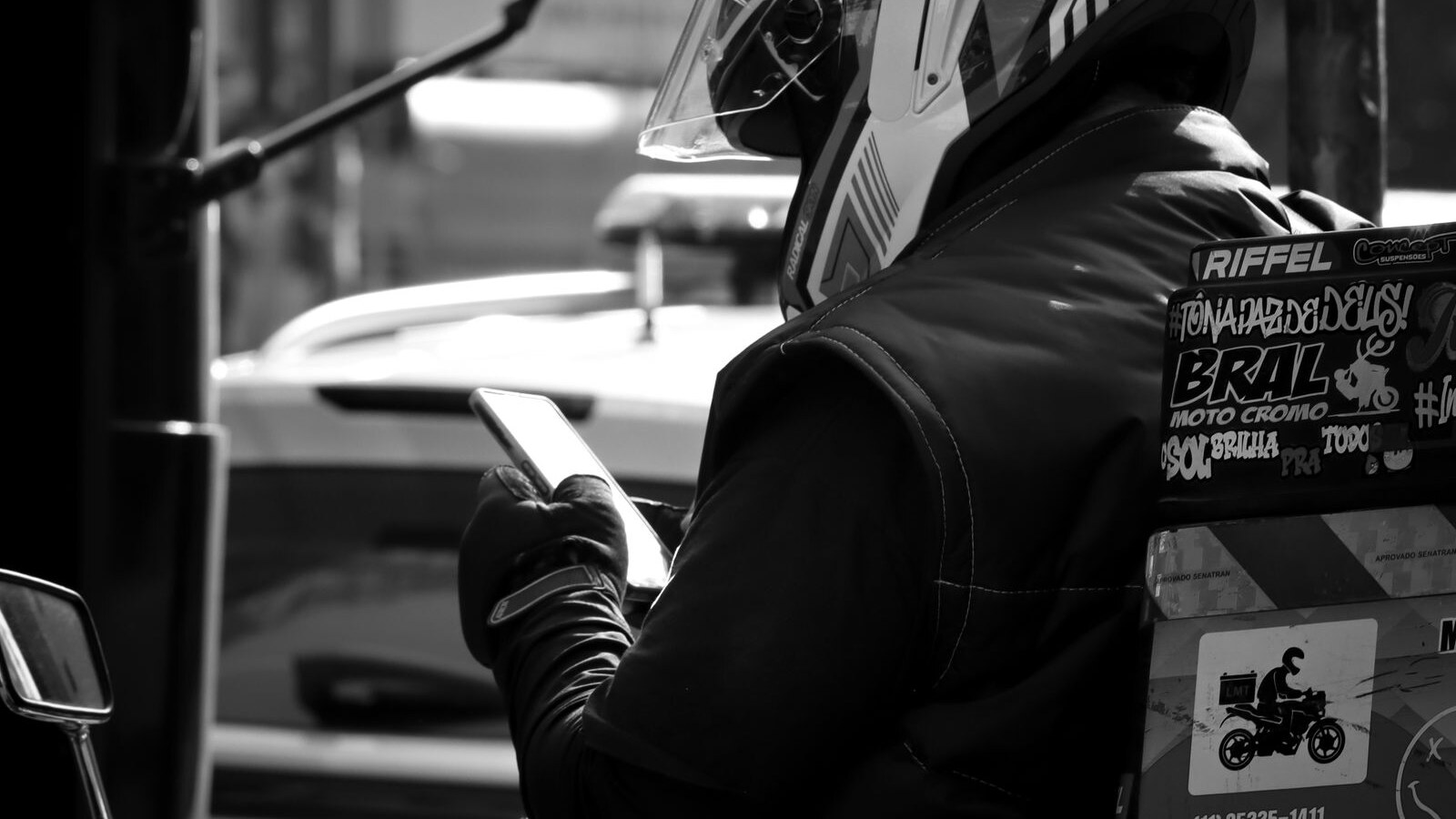 Trabalhador de motocicleta usando o celular em uma via urbana